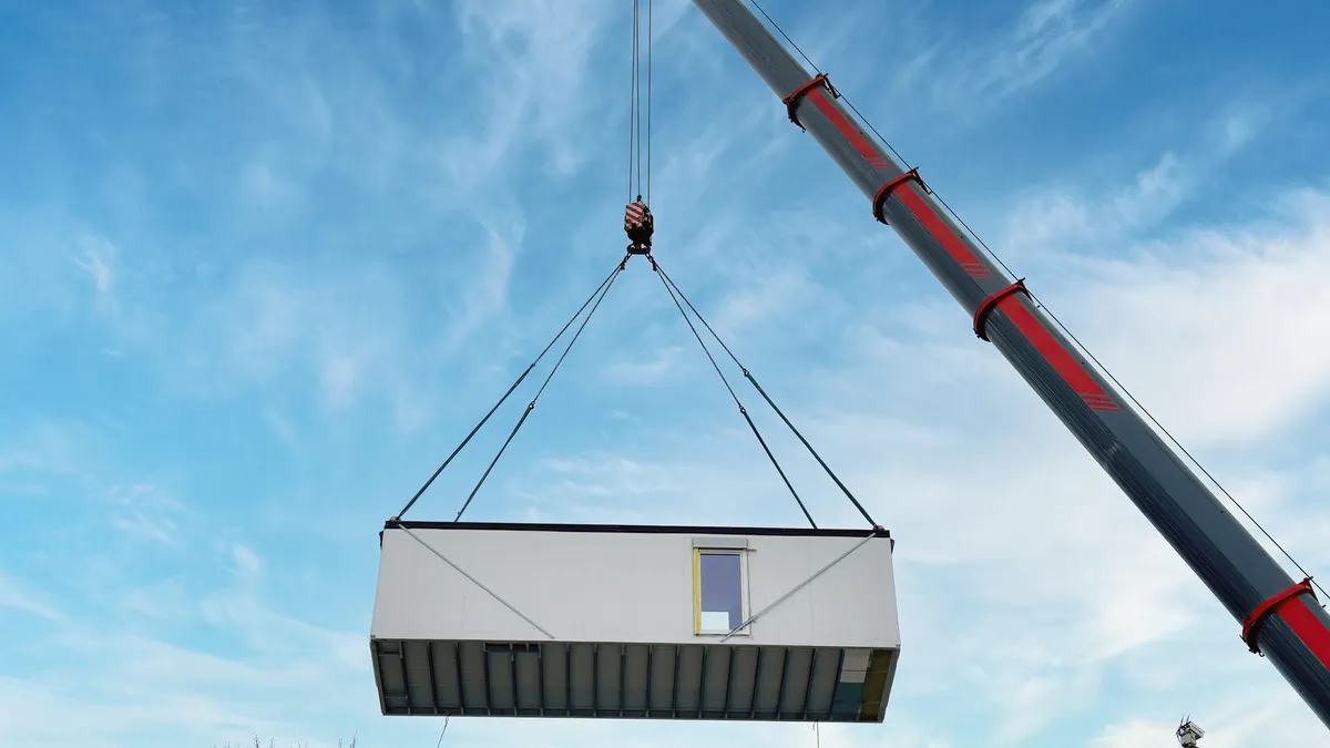 A modular building unit is lifted by a crane.