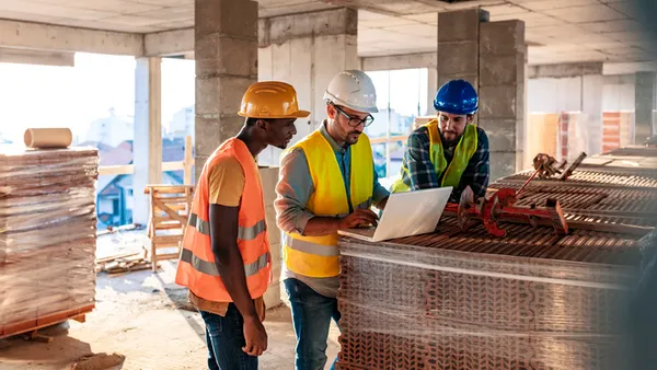 A group of construction stakeholders stand on site and discuss building plans.