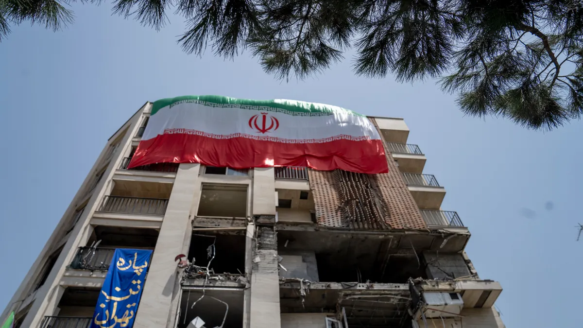 An Iranian flag hangs on the side of a damaged building