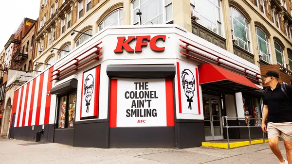 A pedestrian strolls by a KFC ad that shows Colonel Sanders scowling.