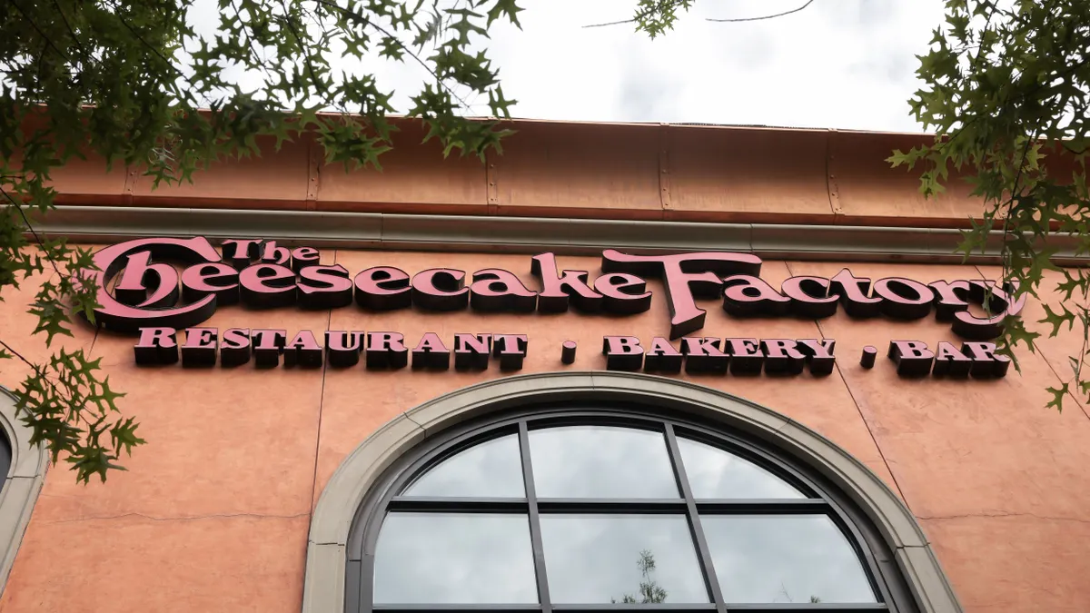Cheesecake Factory signage hangs on the side of a restaurant.