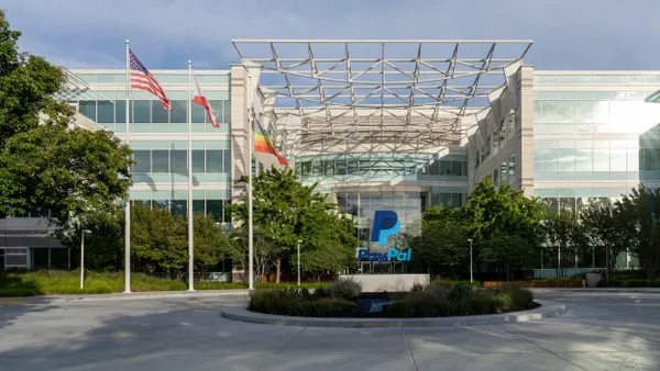 A commercial building stands behind a circular driveway with a monument of the PayPal logo and a sign displayed in the center. 