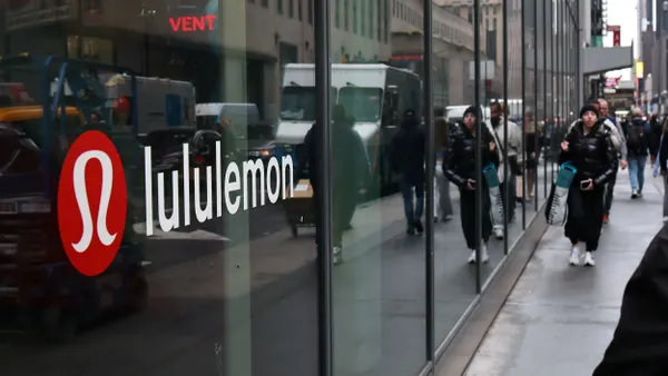 A lululemon logo displayed through a window as people walk by.