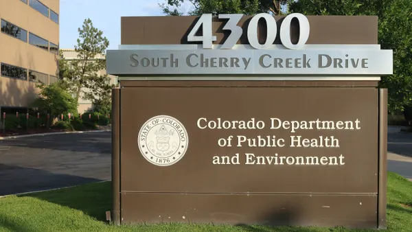 A sign in front of an office building with the state seal has the Colorado state seal and address.