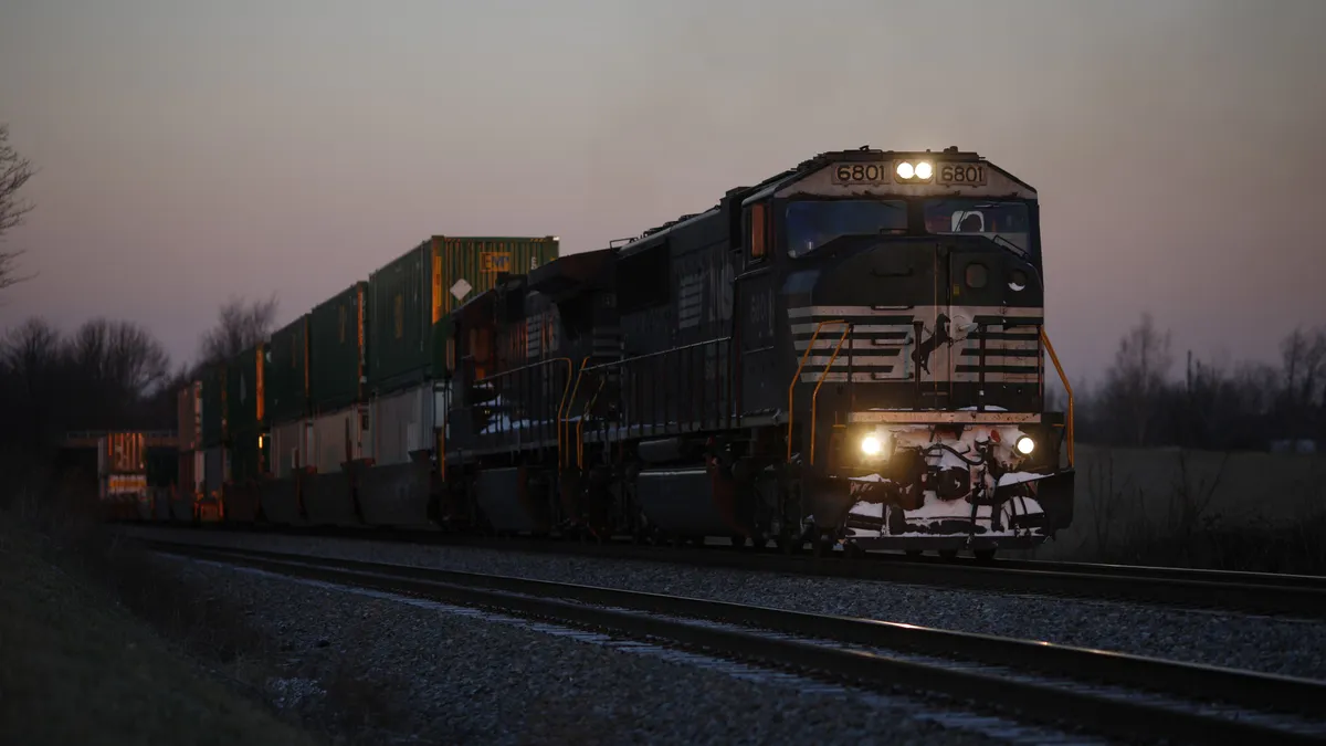 A silver train carrying stacks of containers is seen at sunrise.