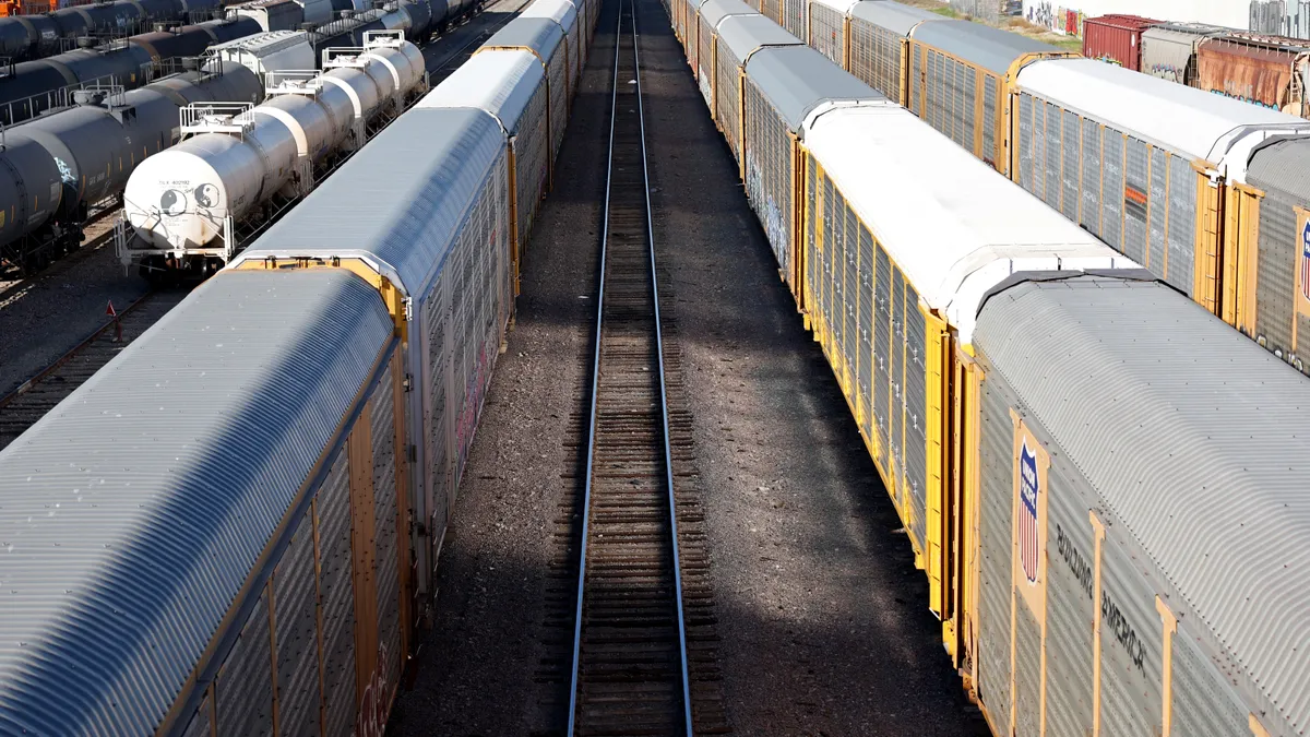 Grey and yellow freight rail cars sit in a rail yard with a line of railroad tracks between them.