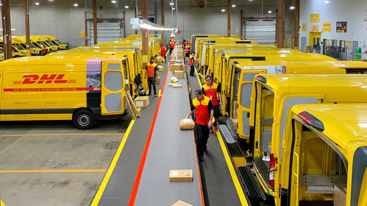 DHL delivery vehicles sit on either side of a long conveyor belt which transports packages down the line.