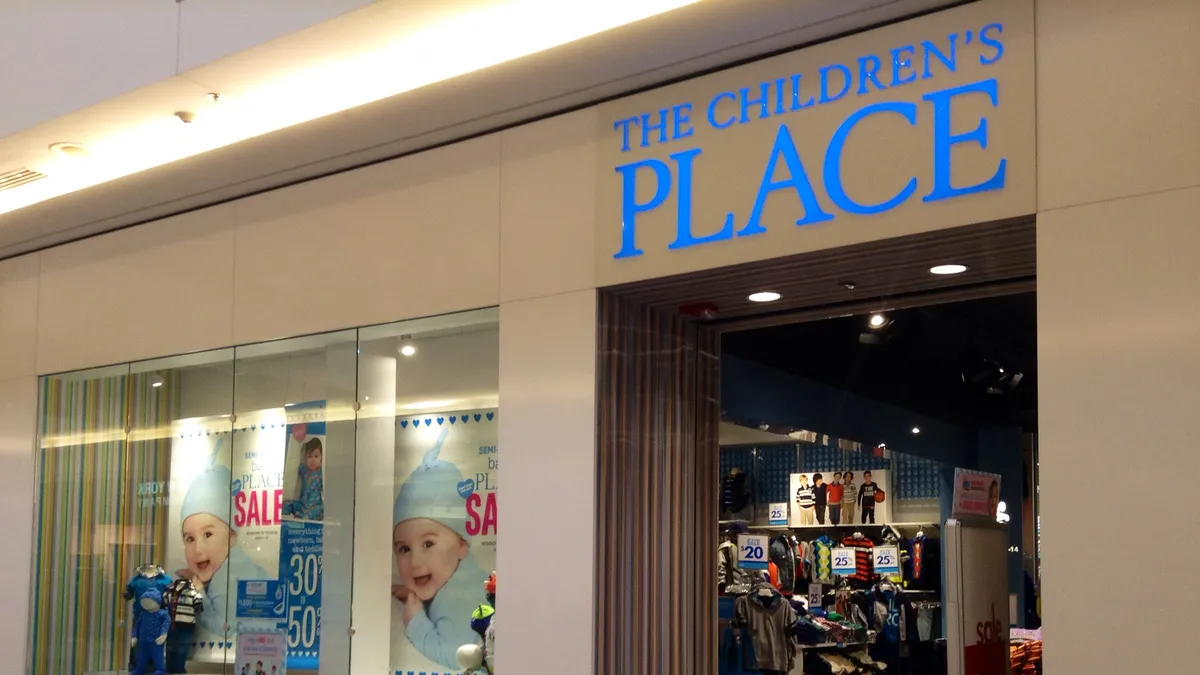 A Children's Place storefront is pictured in a mall, with signs advertising a sale.