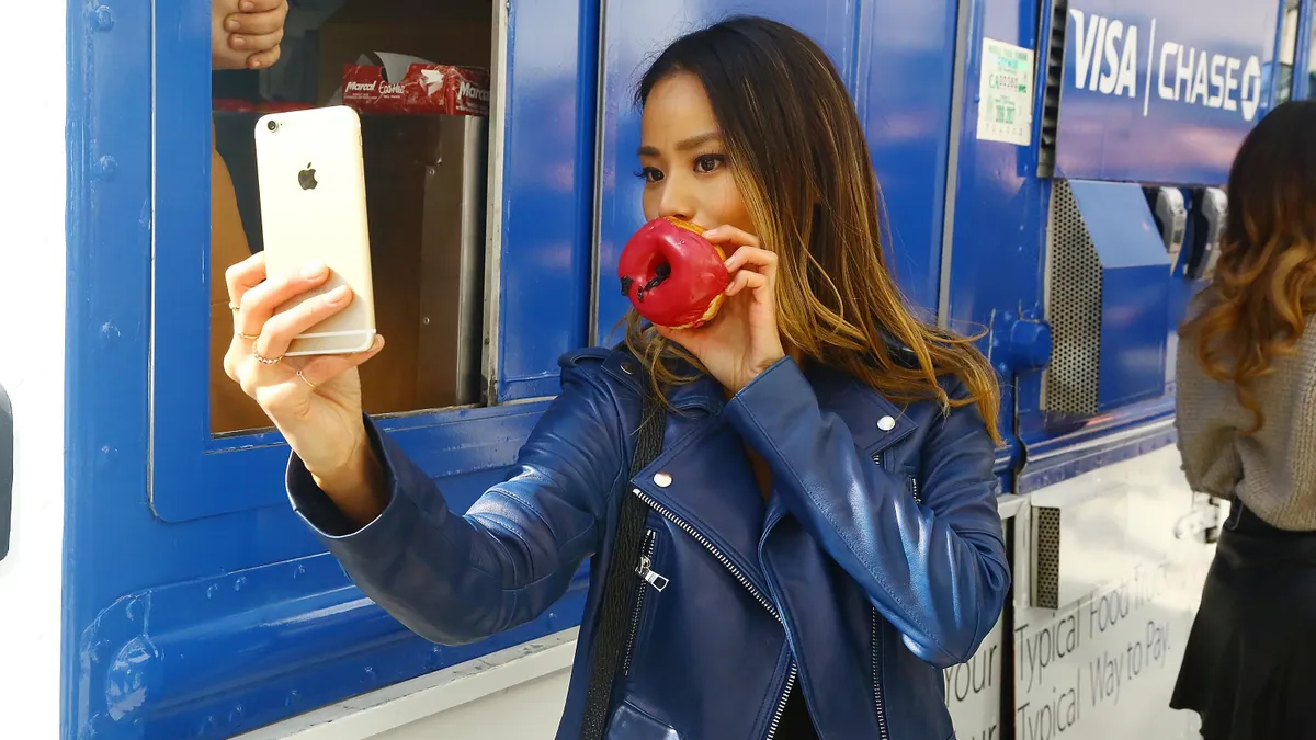 Celebrity Jamie Chung taking a selfie with a donut in front of a food truck in New York City