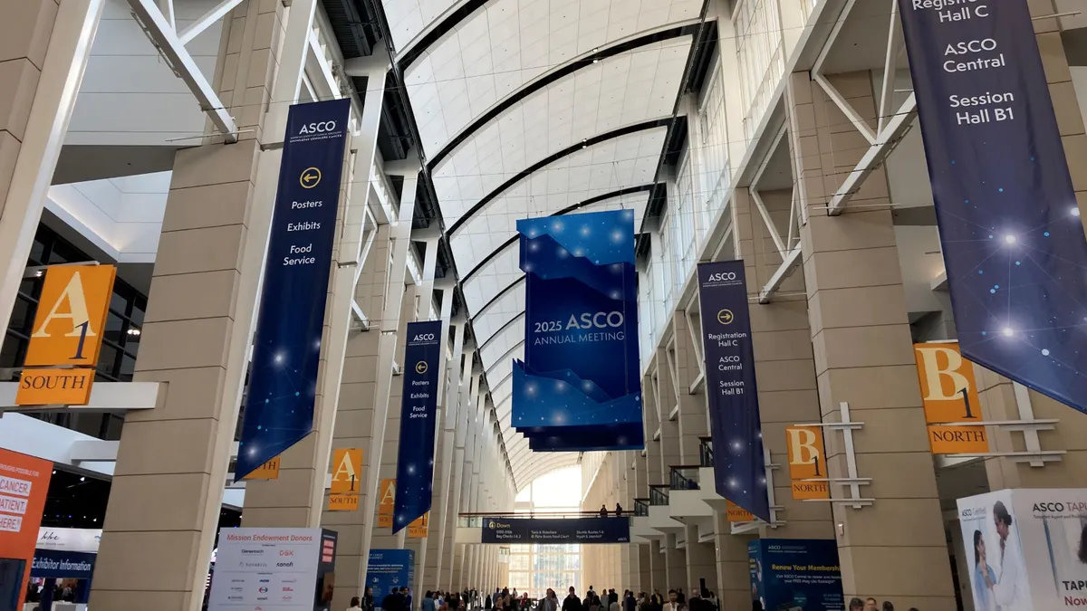 Banners marking the 2025 American Society of Clinical Oncology's annual meeting hang from the ceiling of a conference hall.