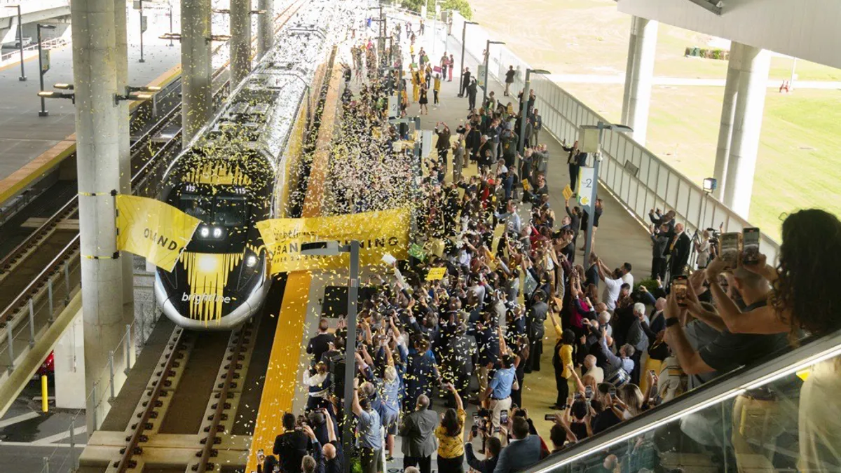 An overhead view of a Brightline train breaking through a banner while confetti flows at the new Orlando, Florida station.