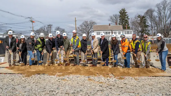 People with hard hats stand with shovels in a pile of dirt.