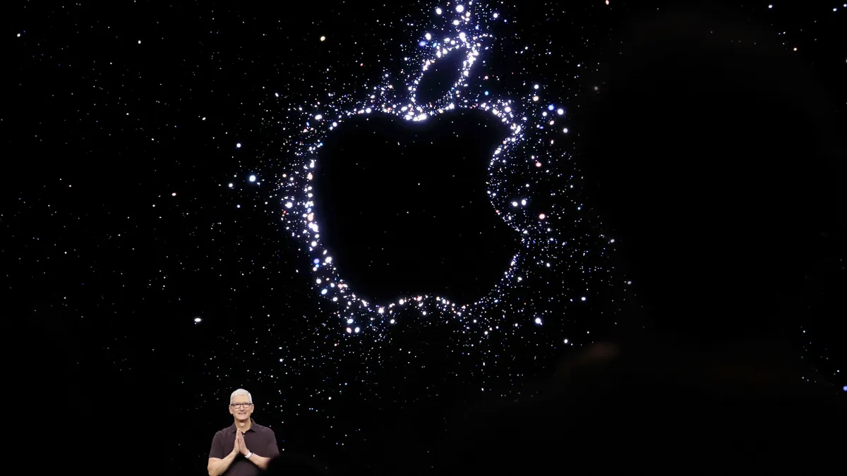 A man standing in front of a black background with the outline of the Apple logo