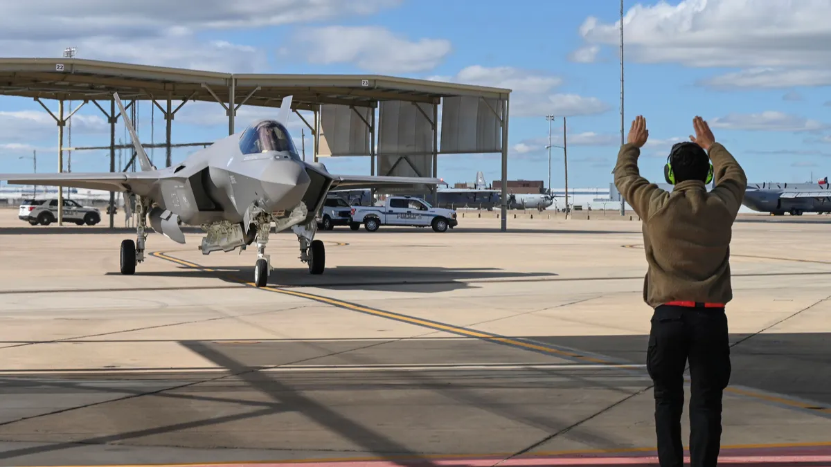 An aircraft marshaller directing a fighter jet into a hangar.