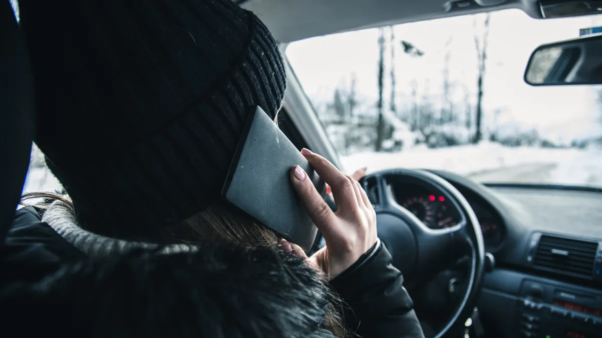 A driver holding a cell phone on a winter road.