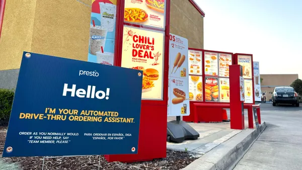 An image of a blue sign in the foreground says "Presto Hello! I'm your automated drive-trhoug ordering assistant." In the background, there are red menu signs and a speaker box for a Wienerschnitzel restaurant drive-thru.