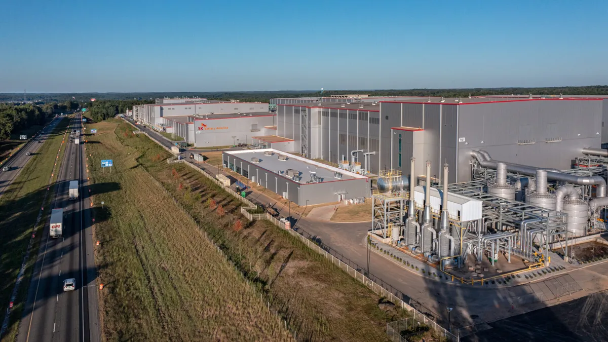 A large silver factory next to a highway with cars.