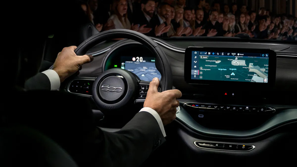 A driver hands are visible sitting behind the wheel of a 2025 Fiat 500e electric car.