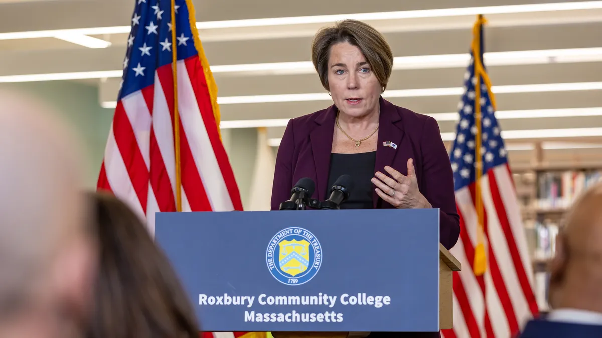 A woman with a short hair cut speaks at a podium that say "Roxbury Community College Massachusetts."