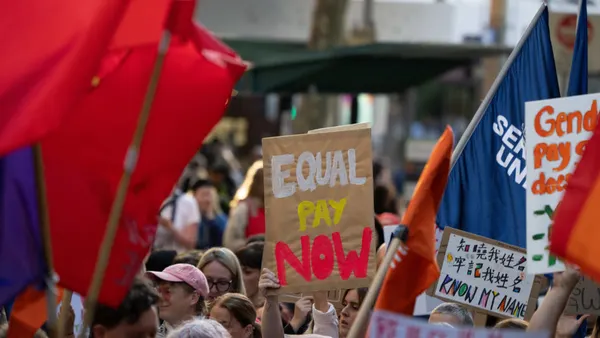 Protestors hold signs saying "Equal Pay Now."