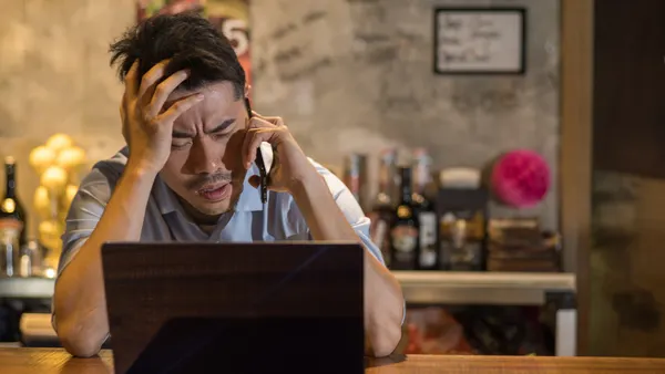 Person talking on phone and looking at computer with expression of frustration.