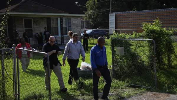 A group of people walk through an open gate with a lawn and stone house behind them.
