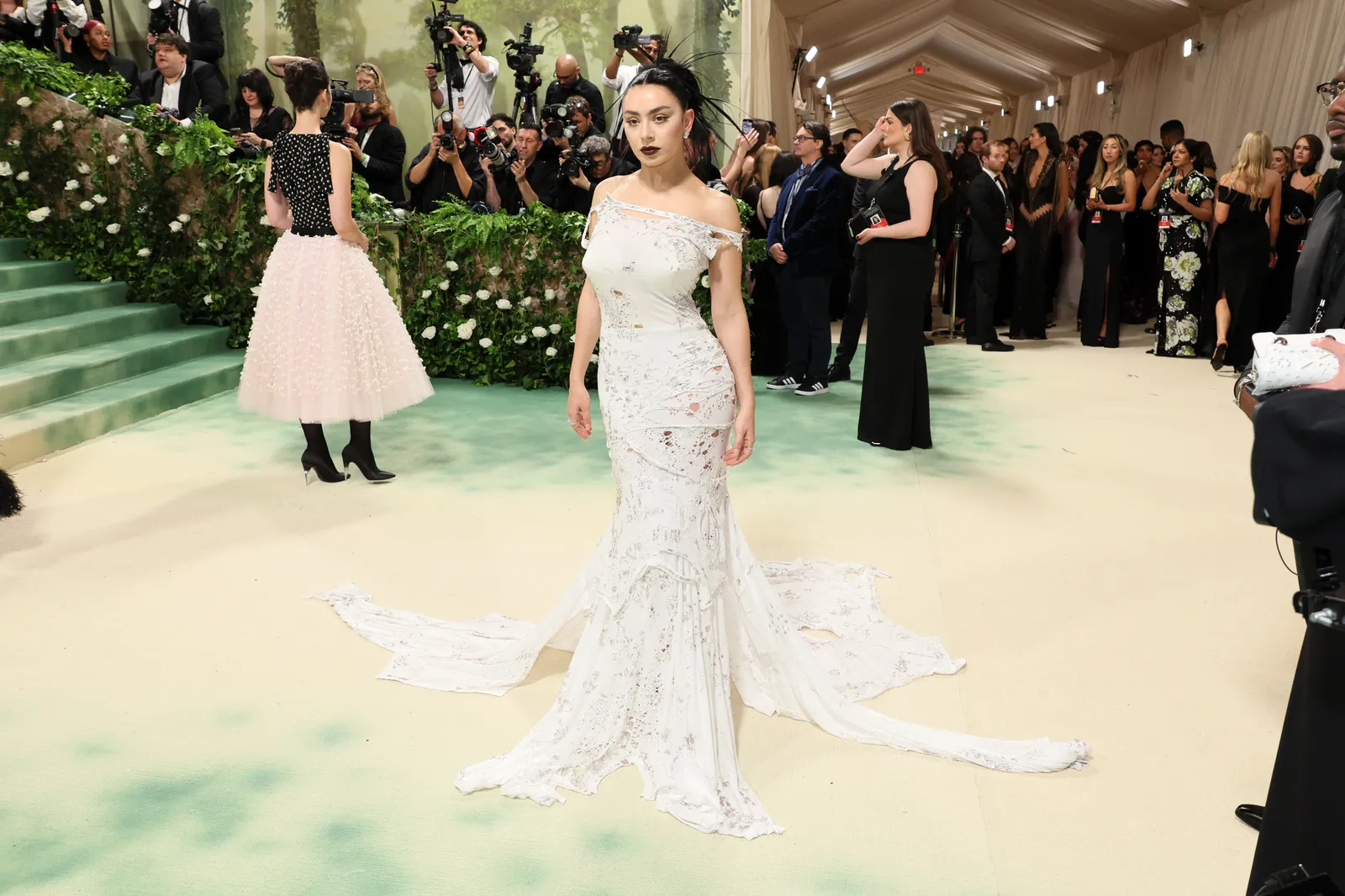 A person in a white gown stands in front of photographers.