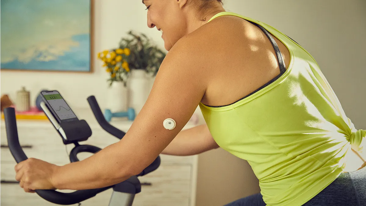 A person on a stationary bike wears a small, white patch on their upper arm.