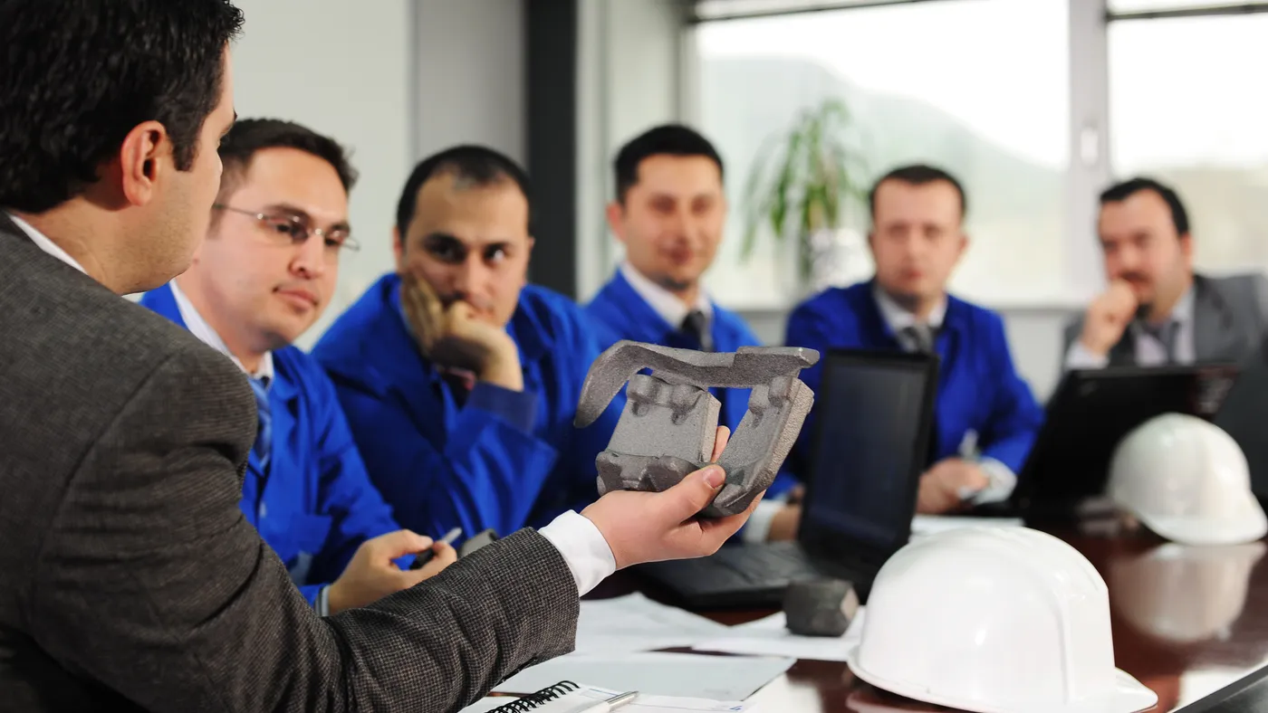 A man displays displays a component around a conference table.