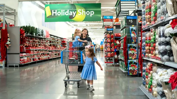 An adult and two children with a shoppiing cart, in a store, surrounded by holiday merchandise.