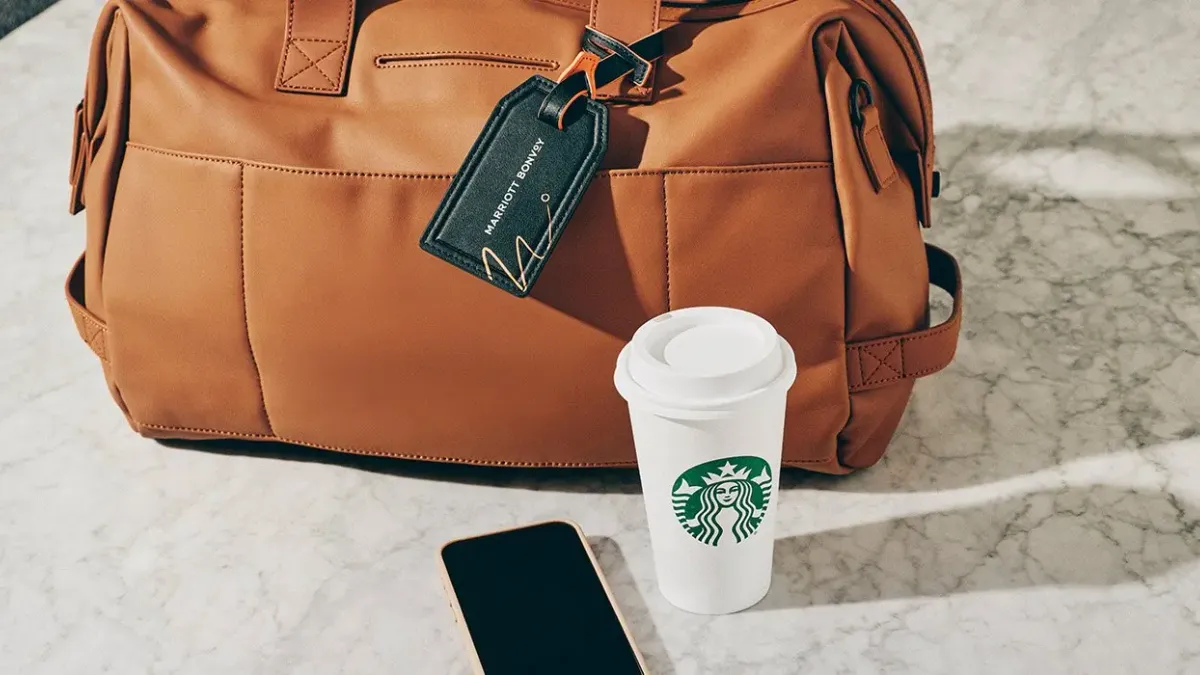 A leather bag with a Marriott Bonvoy tag beside a Starbucks cup and a smartphone.