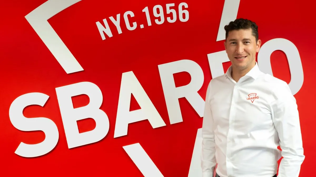 A man stands in front of a red wall with "Sbarro" branding