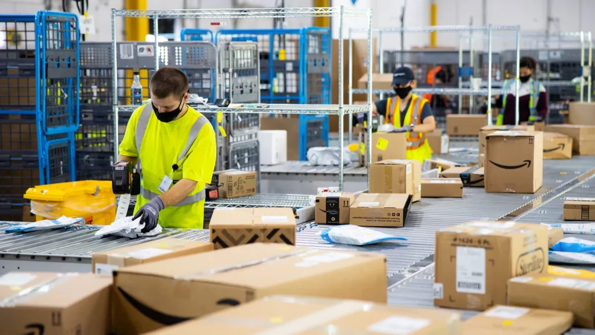 Three Amazon workers in a warehouse prepare orders.