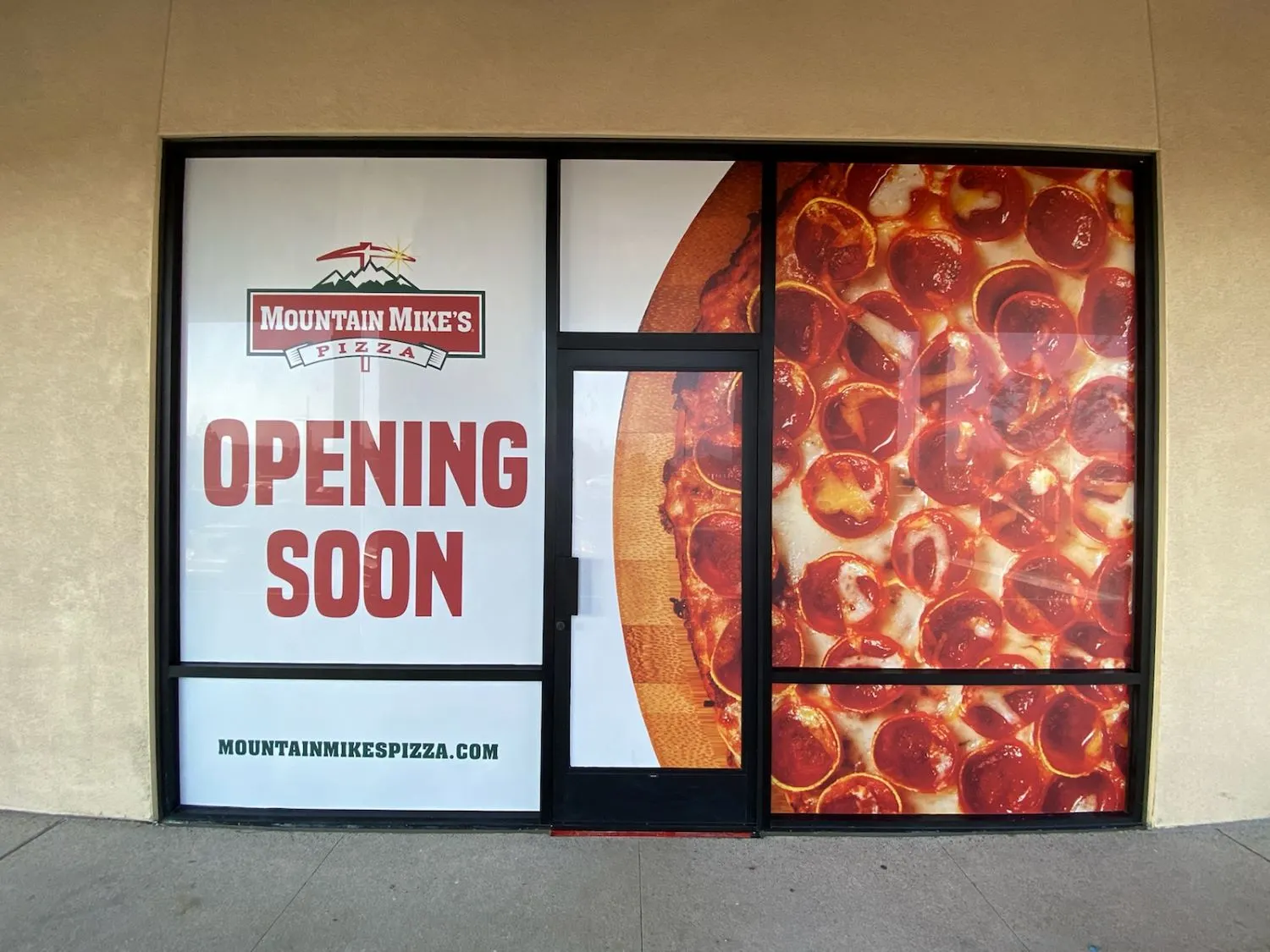A beige building with a bank of windows and a sign covering the windows says "opening soon"