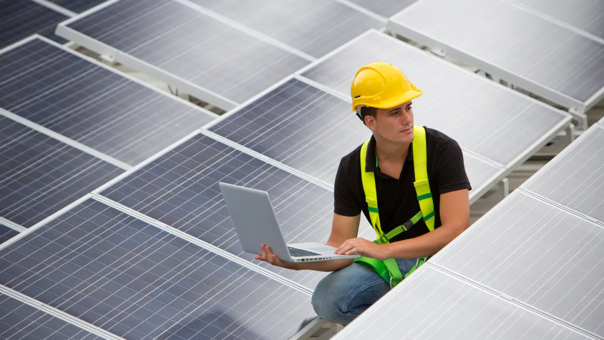 Image of a worker in between photovoltaic panels holding a laptop