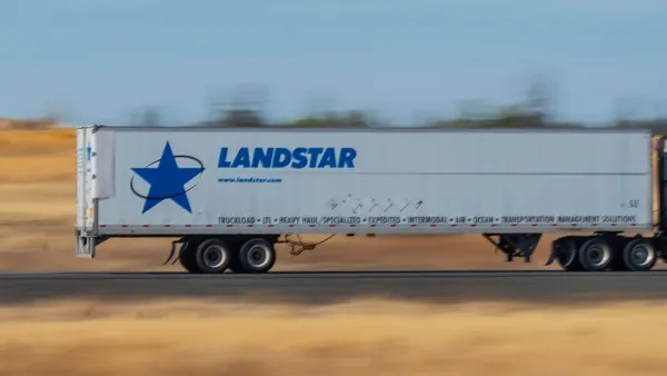 A Landstar System trailer on an interstate with blue sky and a blurred landscape in the background.