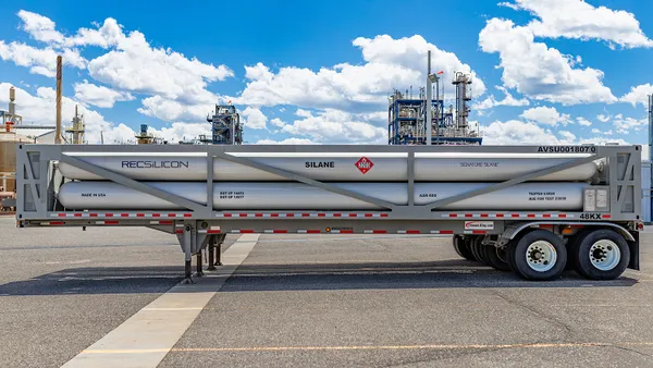 A silver tank parked in front of an outdoor chemical facilityl