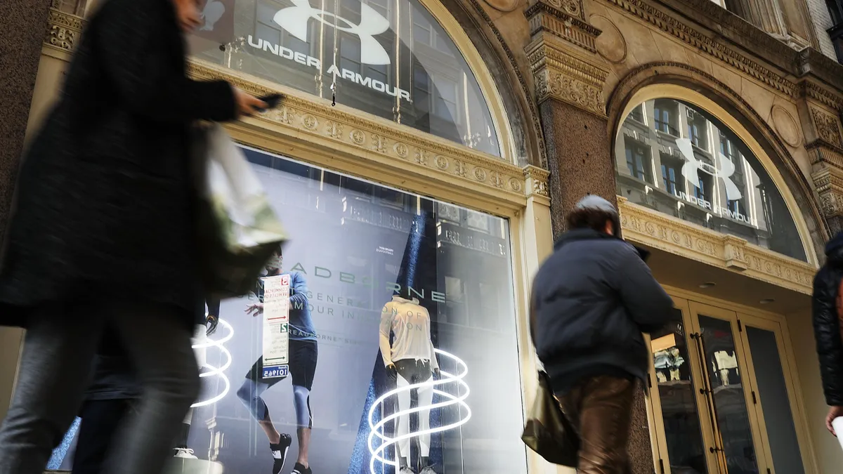 People walk past an Under Armour storefront with mannequins in athleticwear on display.