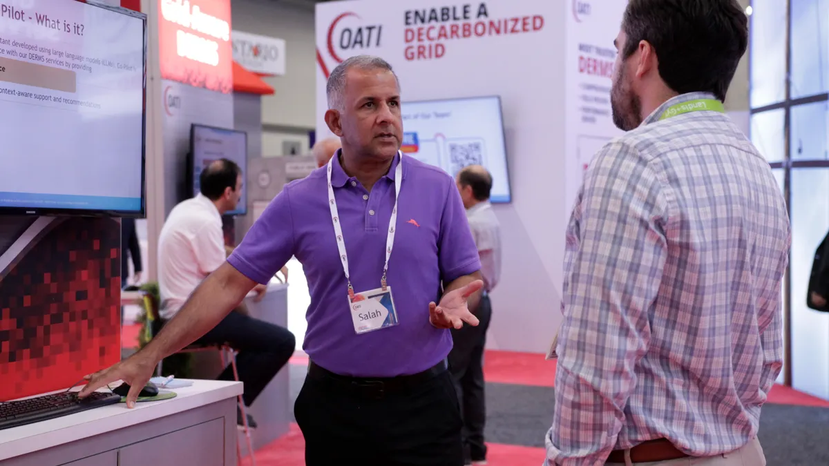 Two men engaged in conversation at a bustling trade show, surrounded by various booths and attendees.