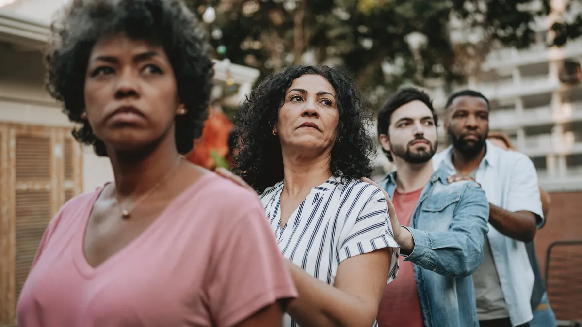 A multi-ethnic group of people stand in an urban area; two women in front, two men in back