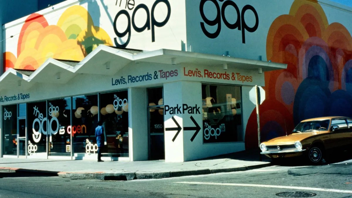 A person window shops at store at a street corner. An orange corner is parked on the right, next to a stop sign.