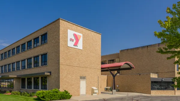An exterior view of a yellow brick two-story building with "The Y" on a sign, taken from a parking lot.