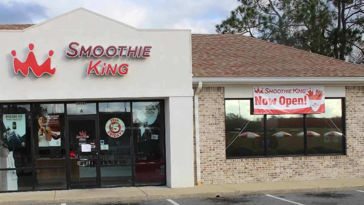 An exterior of a beige building with the words "Smoothie King" in red next to a red crown logo on the outside.