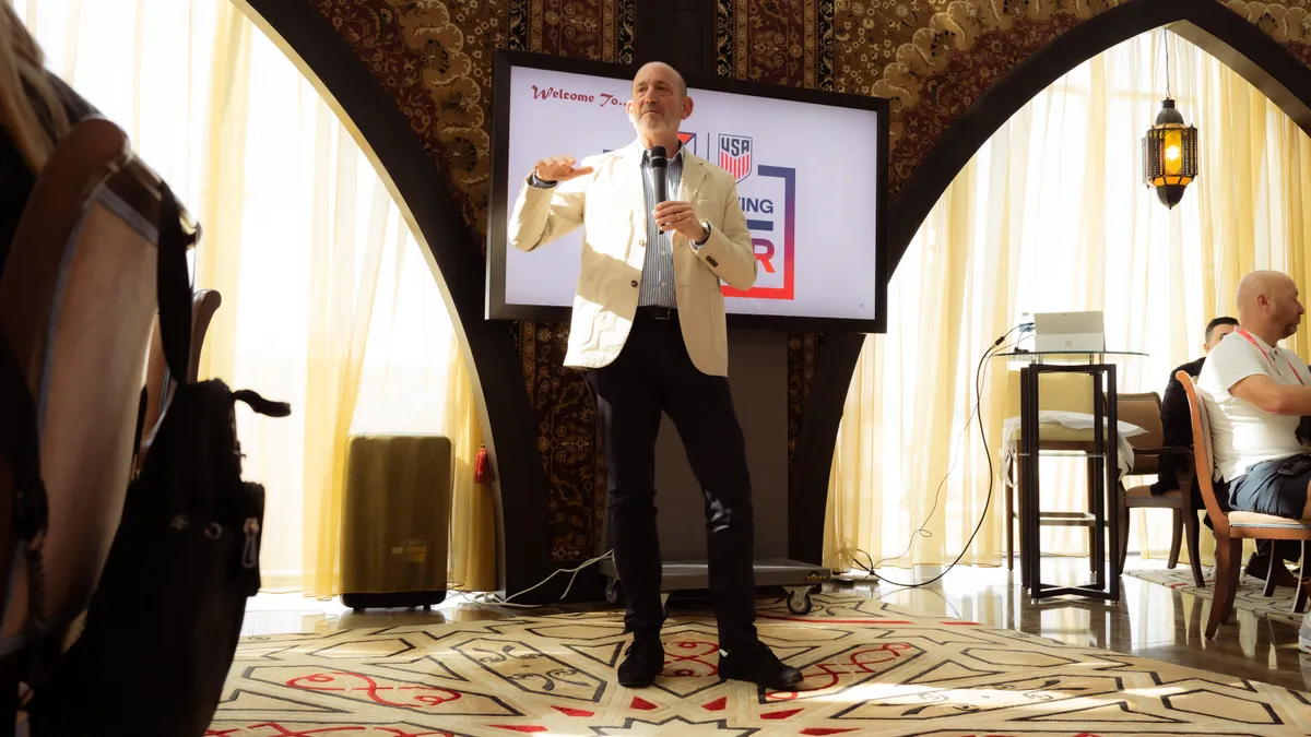 MLS Commissioner Don Garber holds a microphone and speaks in a conference room.