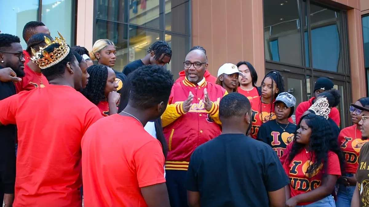 Edington stands on stairs surrounded by students in UDC gear