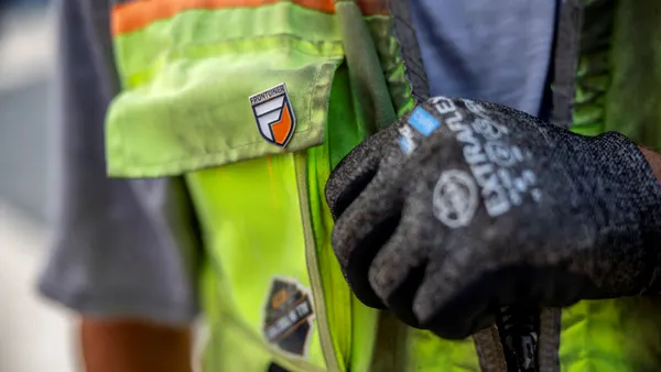 A close-up of a construction worker's vest with a pin on it.