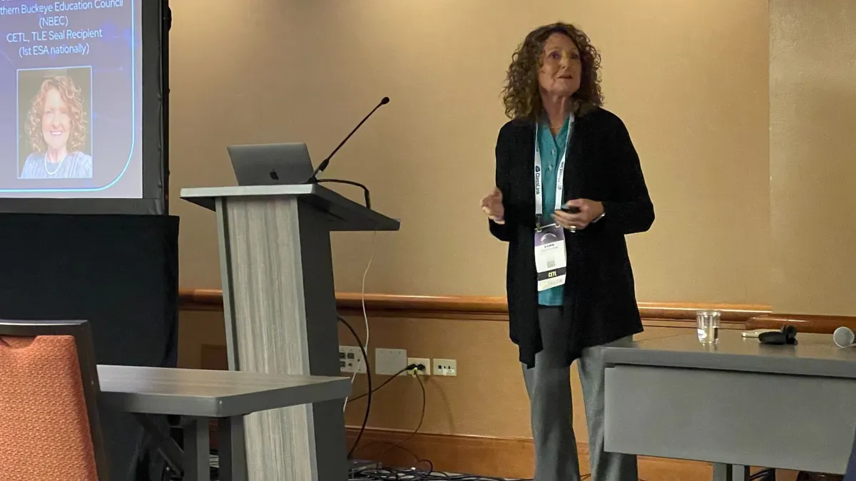 A woman educator is pictured speaking during a session at a professional conference in a hotel meeting room.