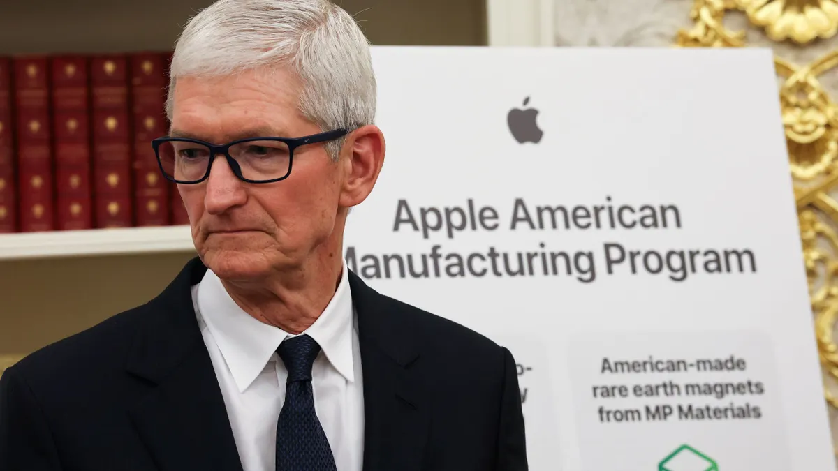A man with white hair and glasses in a black suit looking to the side.