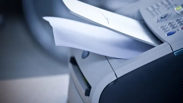 A laser printer with printed documents sits unattended in an office.