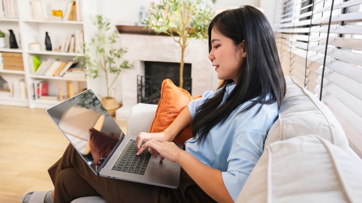 A student works from a laptop while sitting on the couch.